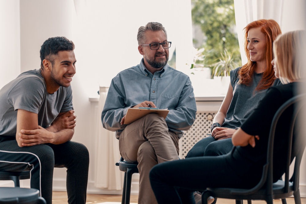 benzodiazepine-rehab-services Male therapist with glasses and clipboard running benzodiazepine addiction treatment group