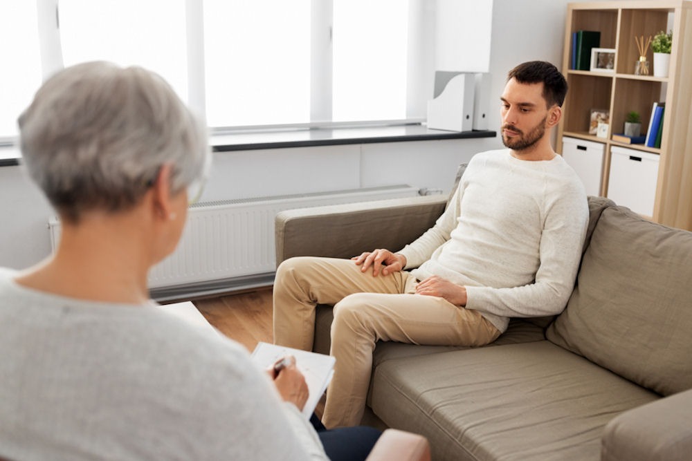 dbt-for-addiction-treatment Sad young man undergoing DBT for addiction with therapist taking notes