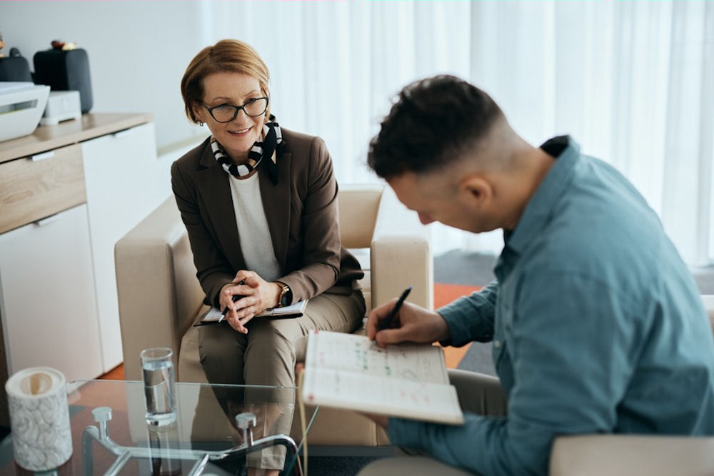 Man signs permission slip for EMDR while smiling therapist looks on, emdr for addiction recovery, insurance verification, licenses and accreditation
