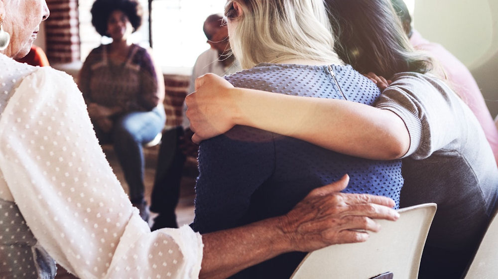 Older woman giving comfort to another younger woman in group therapy setting, family therapy for addiction