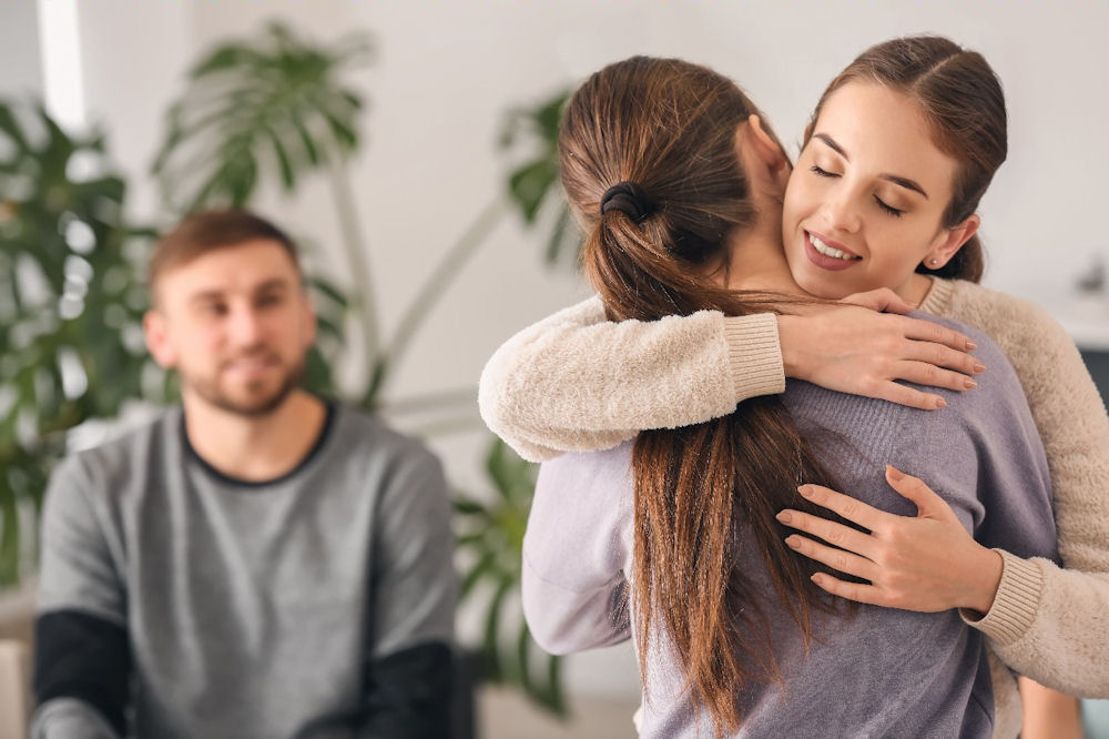 Woman hugging another woman while a man looks on, family therapy for addiction