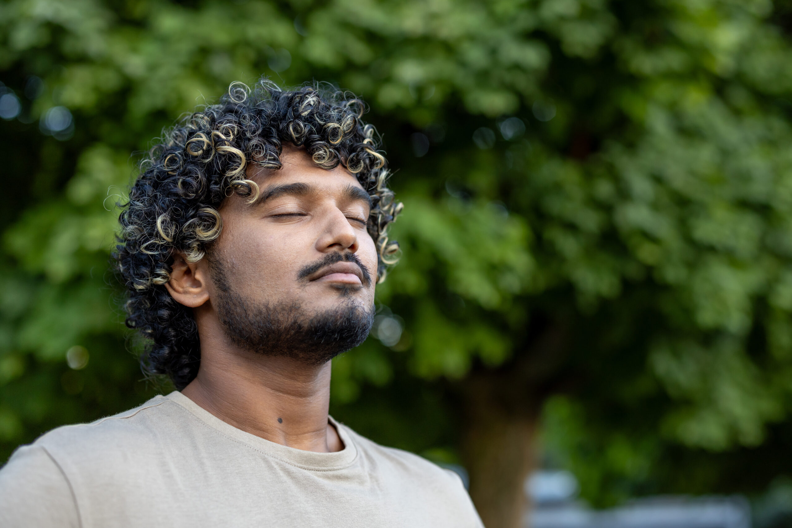 A serene portrait of a man with curly hair enjoying a peaceful moment outside surrounded by green leaves, highlighting relaxation and mindfulness in nature. detox program in san diego,